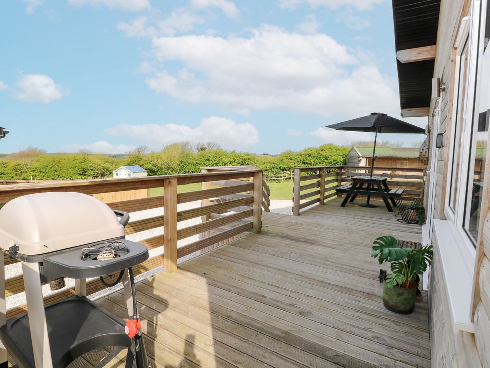 A deck with a grill, table, and umbrella at Monks Rest in Monknash