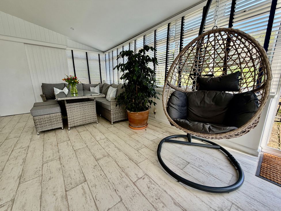 A conservatory with a hanging chair and a sectional sofa at Topsails in Totland Bay