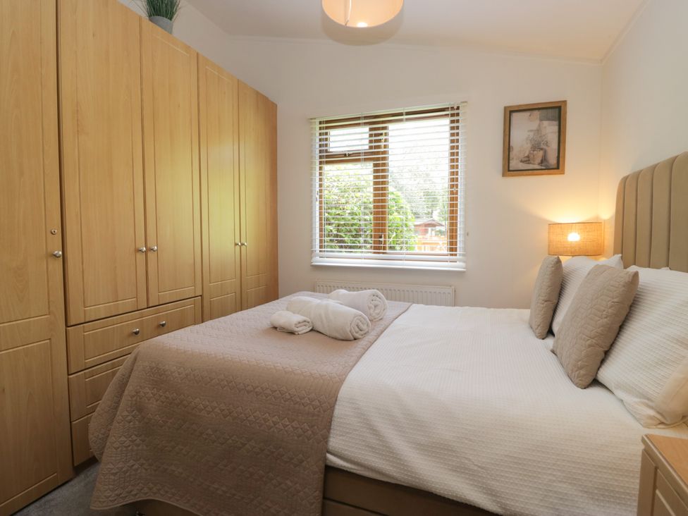 A bedroom with a double bed and wardrobe at Ruskin Lodge, Langdale 16, White Cross Bay near Windermere