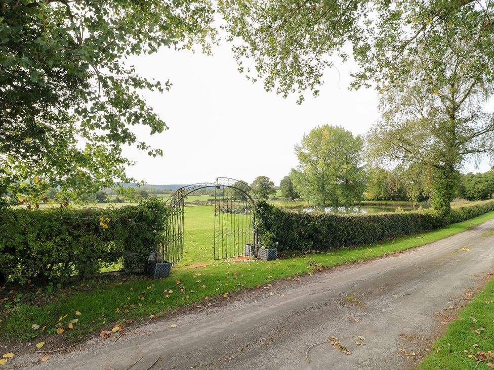 A gate leading to a field with trees and a pond at The Hereford Lodge in Great Haywood