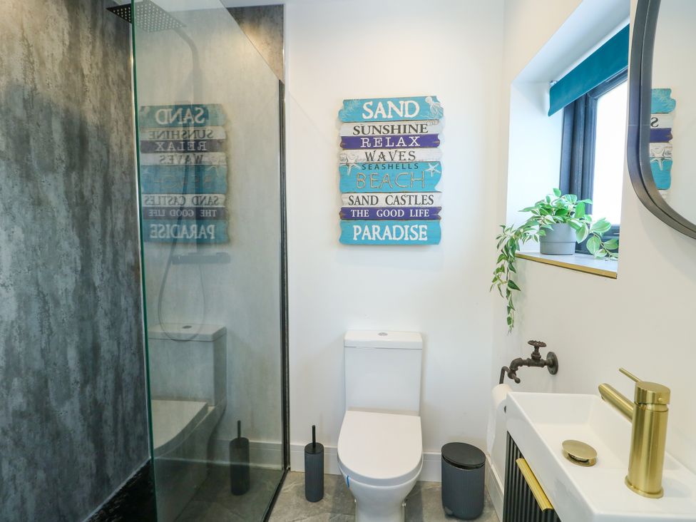 A bathroom with a shower, toilet, sink, and decorative wall sign at Iscoed in Rhosneigr
