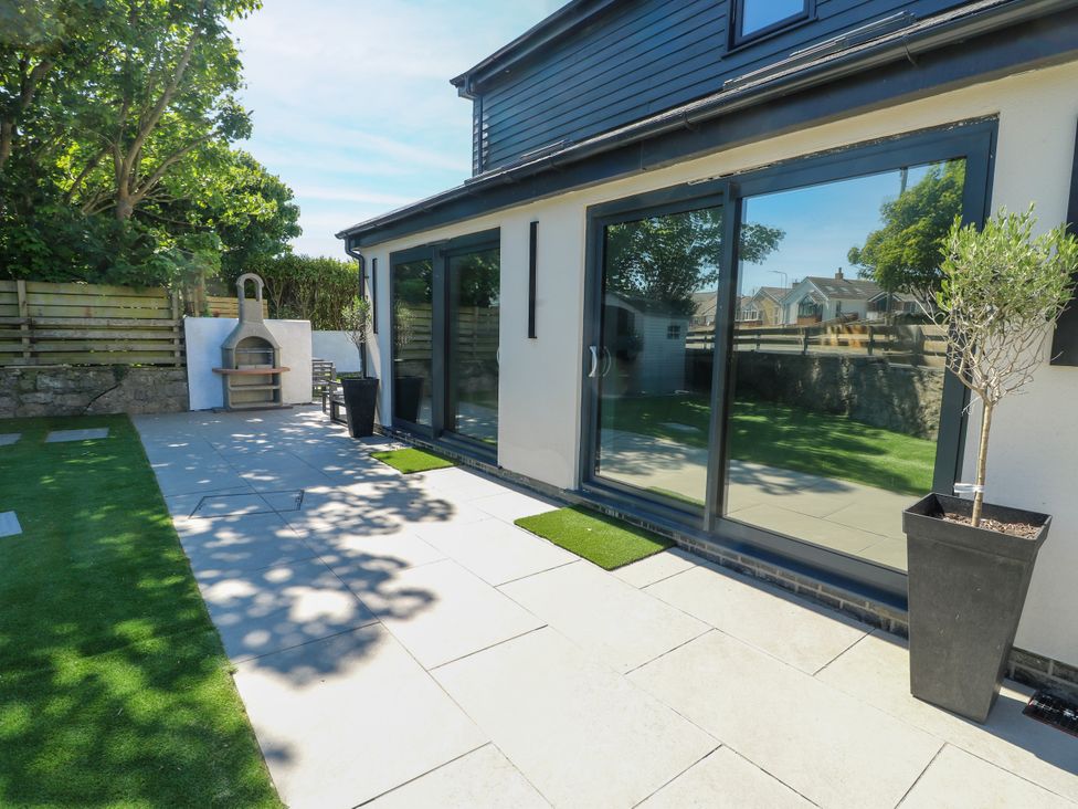 A garden with a patio and sliding doors at Iscoed Rhosneigr