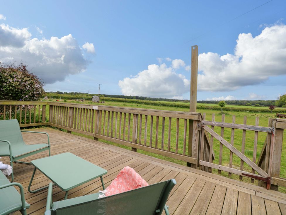A deck with chairs and a table overlooking grass fields at Hollyhock in King's Lynn