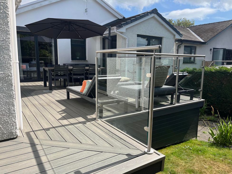 A deck with outdoor furniture and a parasol at Yonder Lea in Bowness-On-Windermere