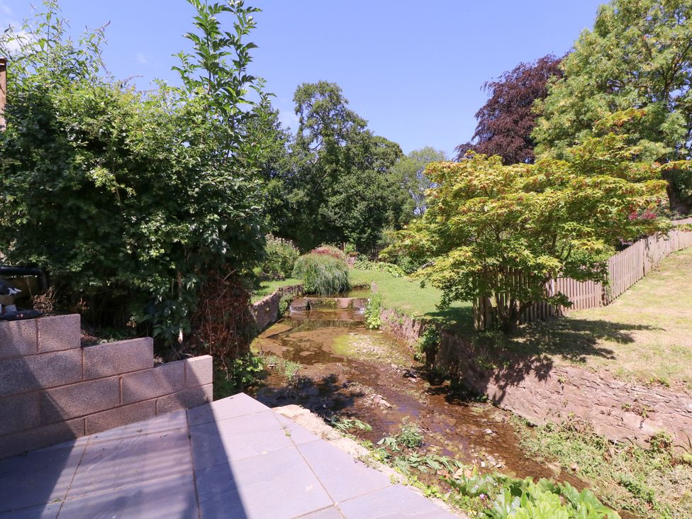 A garden with a stream and trees at Ranbir House in Longhope