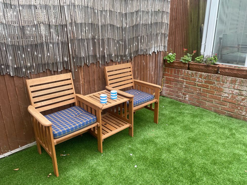 A garden with wooden chairs and a table at Sandy Haven in Swanage