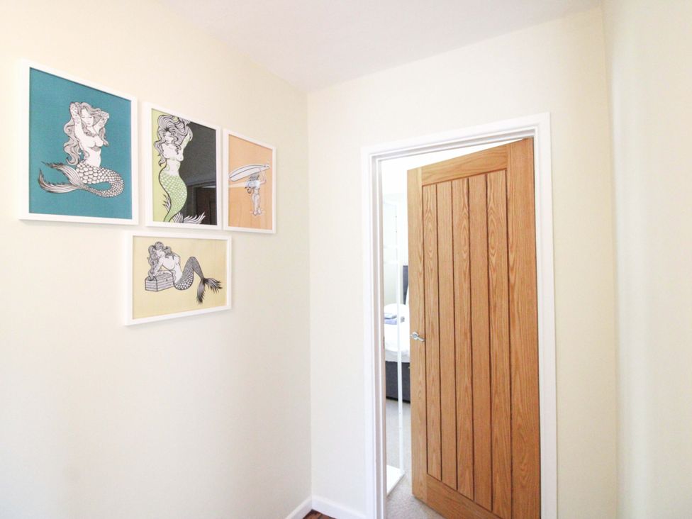 A hallway with framed artwork on the wall and a wooden door at Tansea in Hope Cove