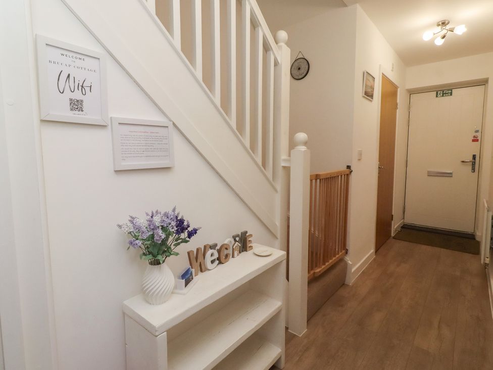 A hallway with a staircase and welcome signs at Brucap Cottage Beadnell