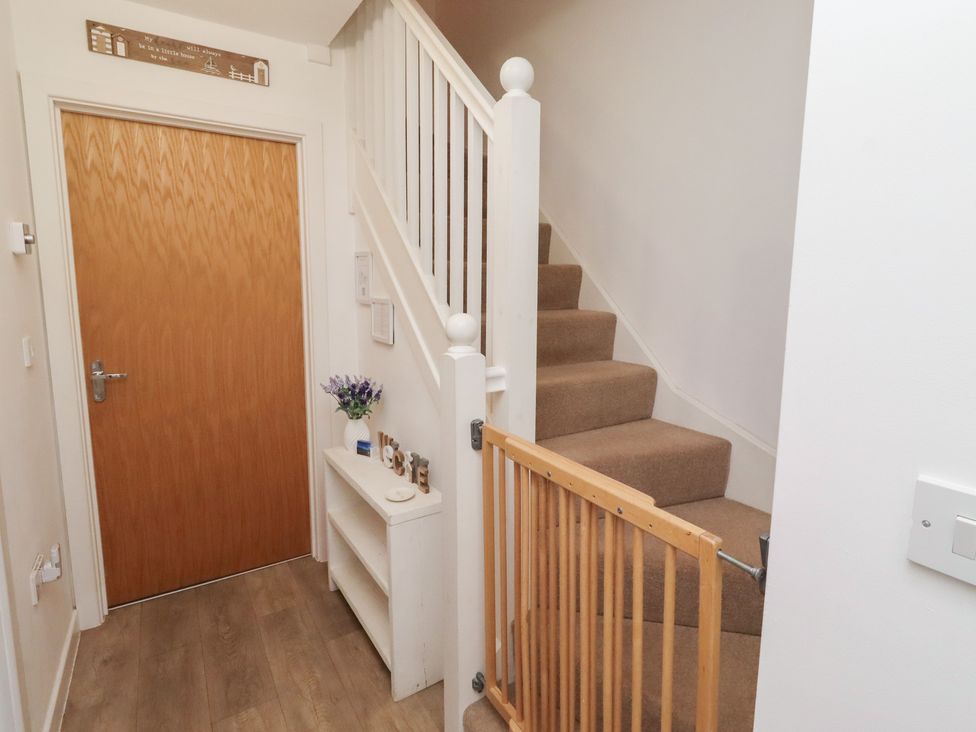 A hallway with a staircase and door at Brucap Cottage in Beadnell