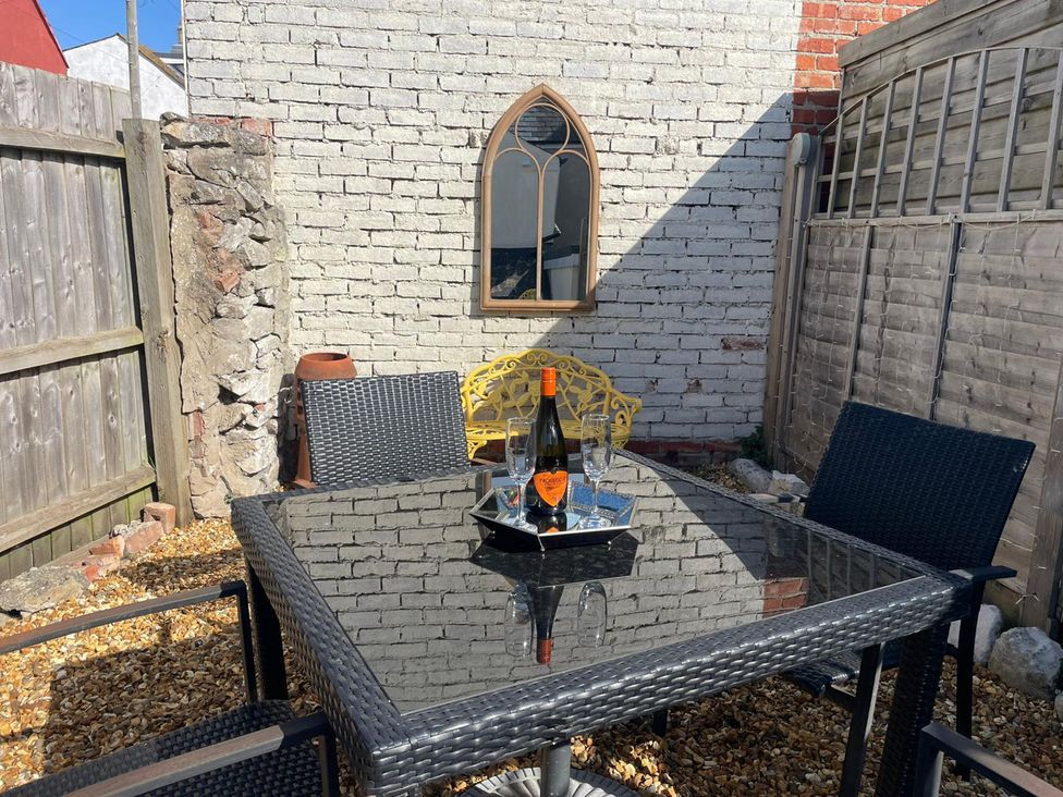 A garden setting with a table and chairs featuring a bottle and glasses at Winkle Cottage in Weymouth