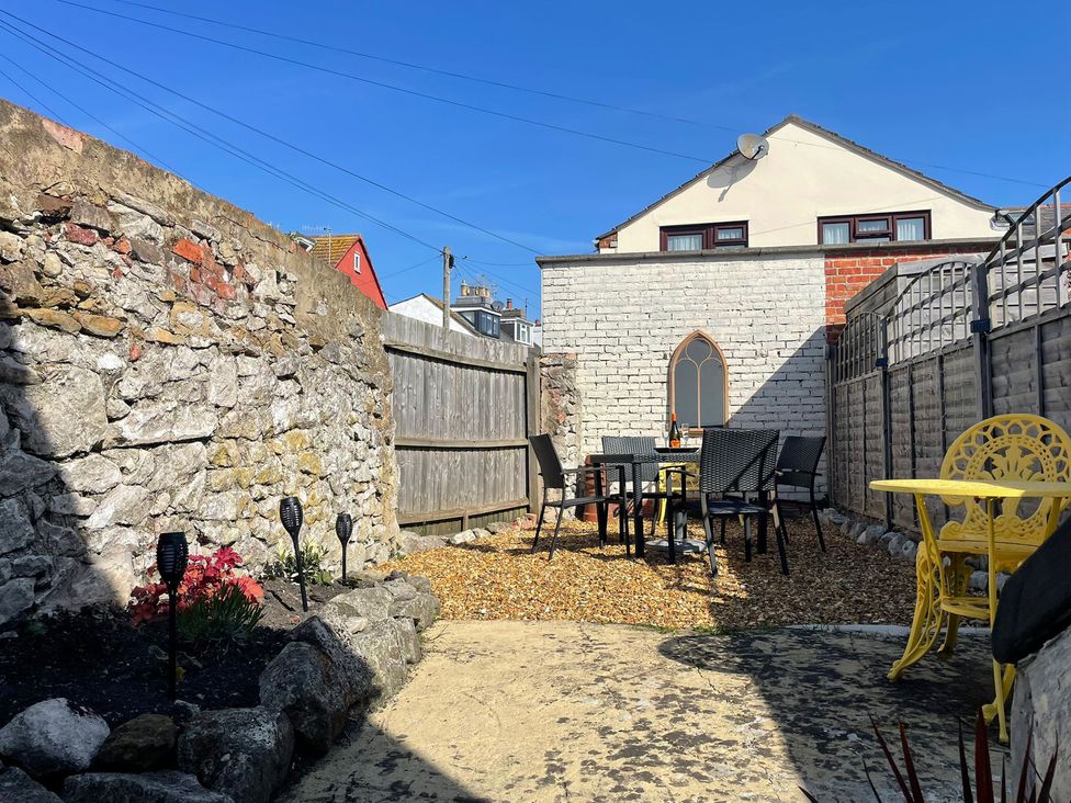 A garden with stone walls and a table with chairs at Winkle Cottage in Weymouth