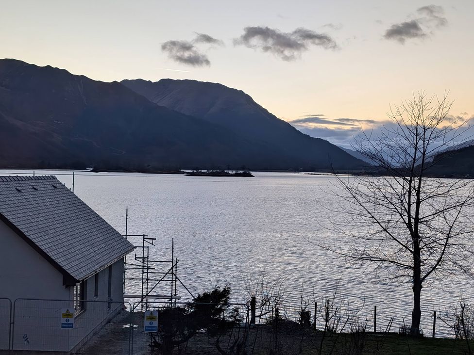 A view of a lake and mountains with a house and tree at Callart View in Glencoe