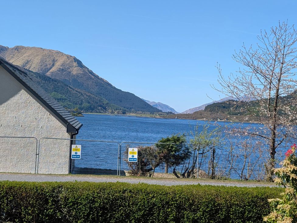 A view of a lake and mountains with a house and fence at Callart View Glencoe