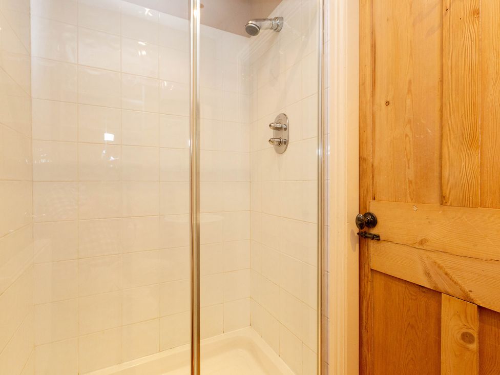A shower with glass enclosure and wooden door at Bod Idris Barmouth