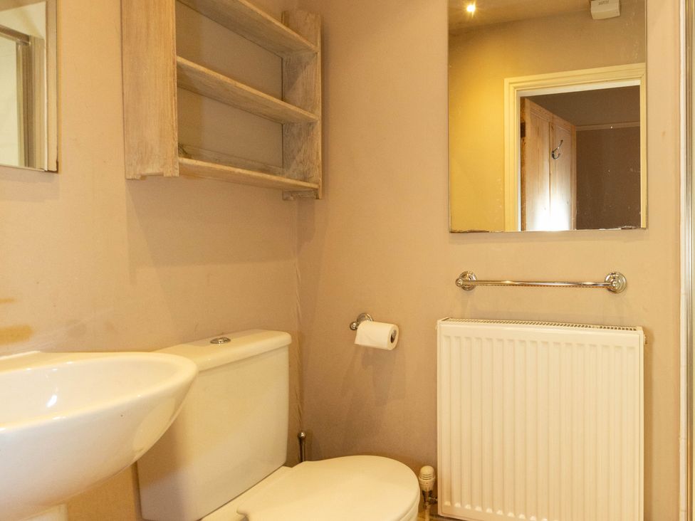 A bathroom with a sink, toilet, mirror, shelves, and towel rail at Bod Idris in Barmouth