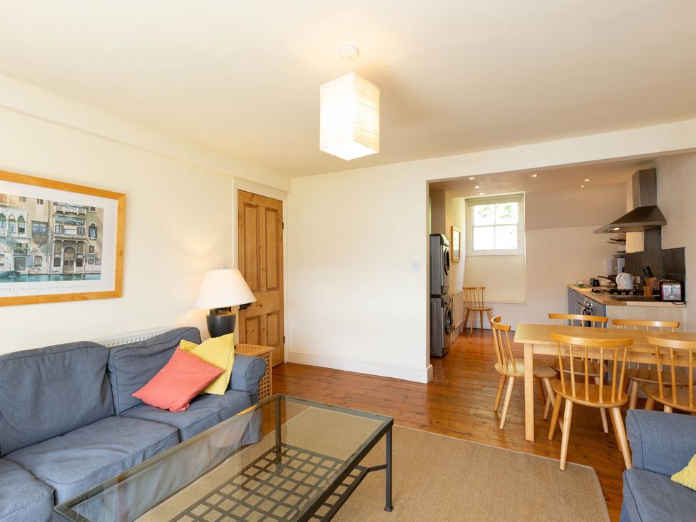 A living room with a sofa and table leading to a kitchen at Bod Idris in Barmouth