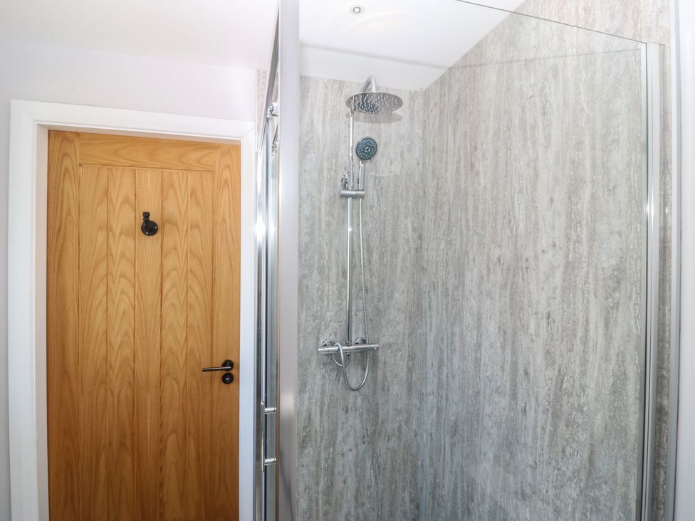 A shower with a glass door and wooden door at The Hideaway in Mynytho near Abersoch