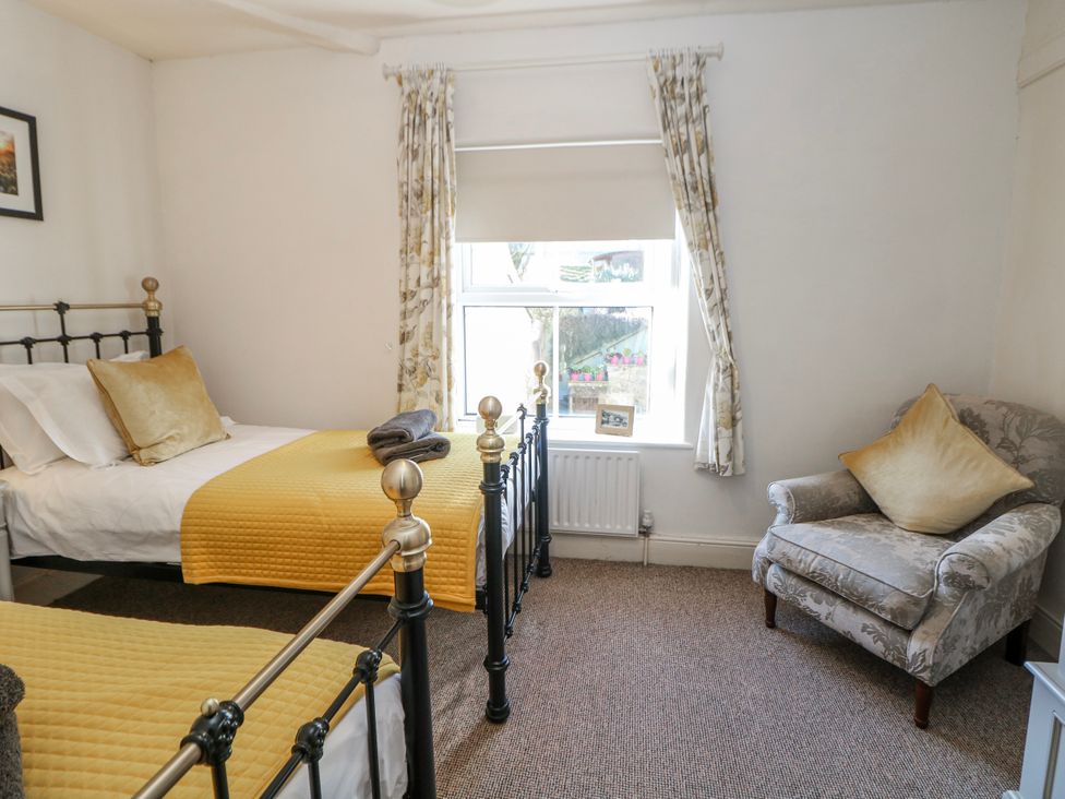 A bedroom with two beds and a chair at Corner Cottage in Tideswell