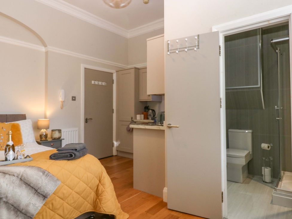 A bedroom with a bathroom door and kitchen amenities at Queens Park in Llandudno