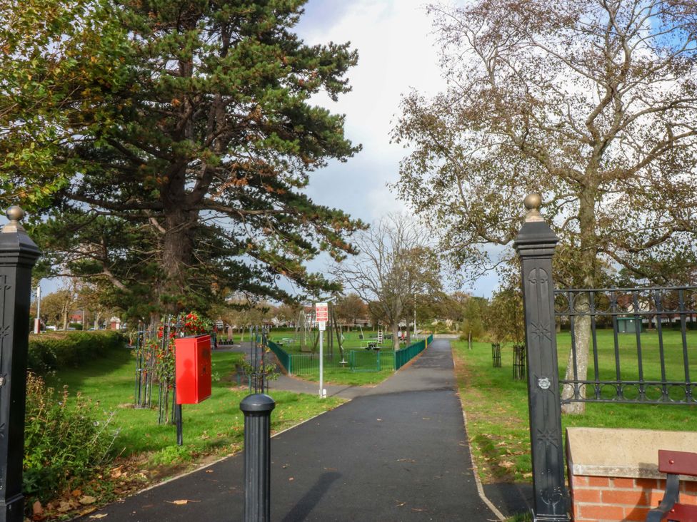 A park entrance with trees and a red postbox at Queens Park in Llandudno