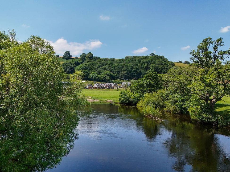 A scenic view of a river with trees and houses in Corwen