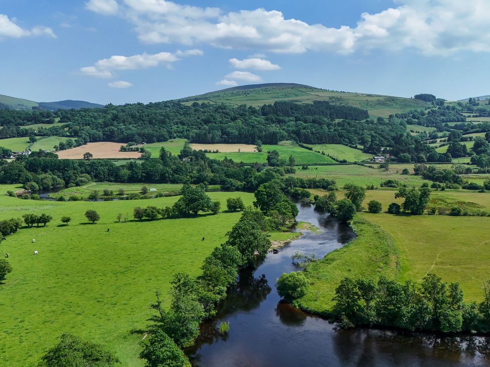 A scenic view of a river surrounded by fields and hills at The Barn in Corwen