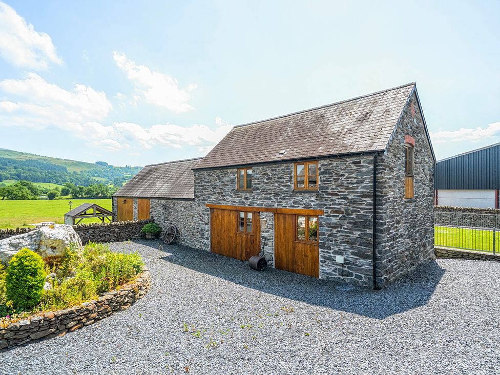 A stone house with wooden doors and a gravel driveway at The Barn in Corwen
