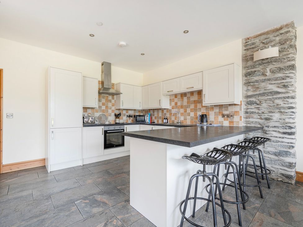 A kitchen with bar stools and appliances at The Barn in Corwen