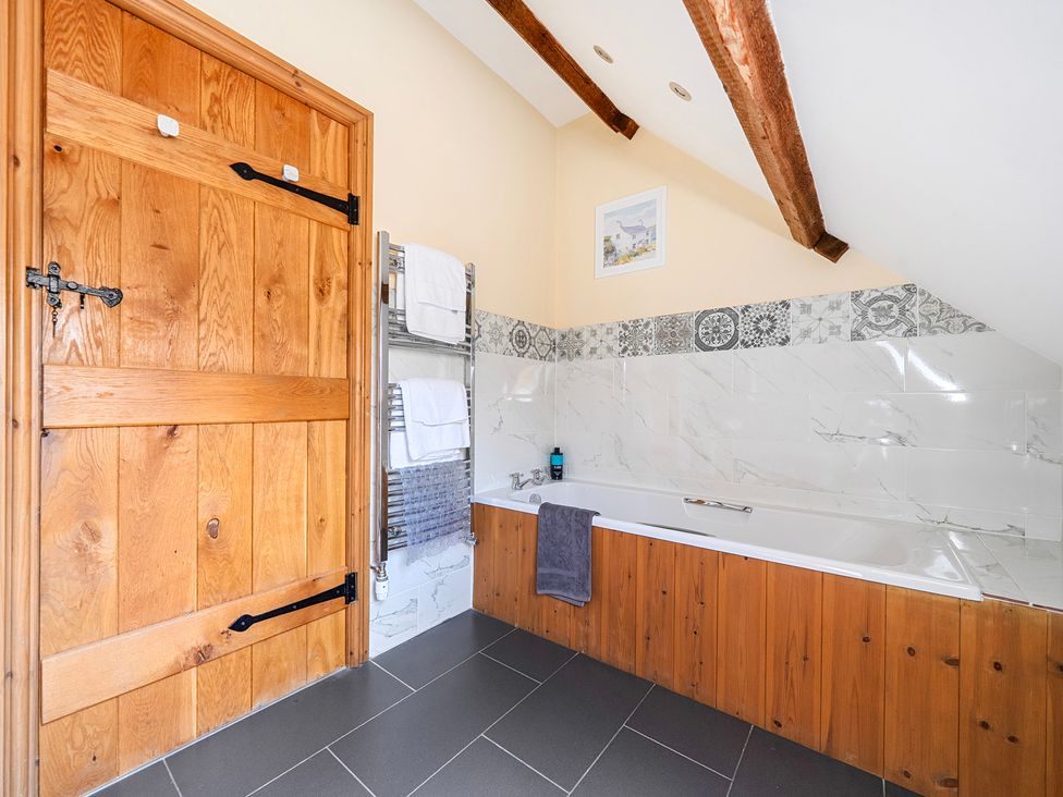 A bathroom with a bath tub and wooden door at The Barn in Corwen