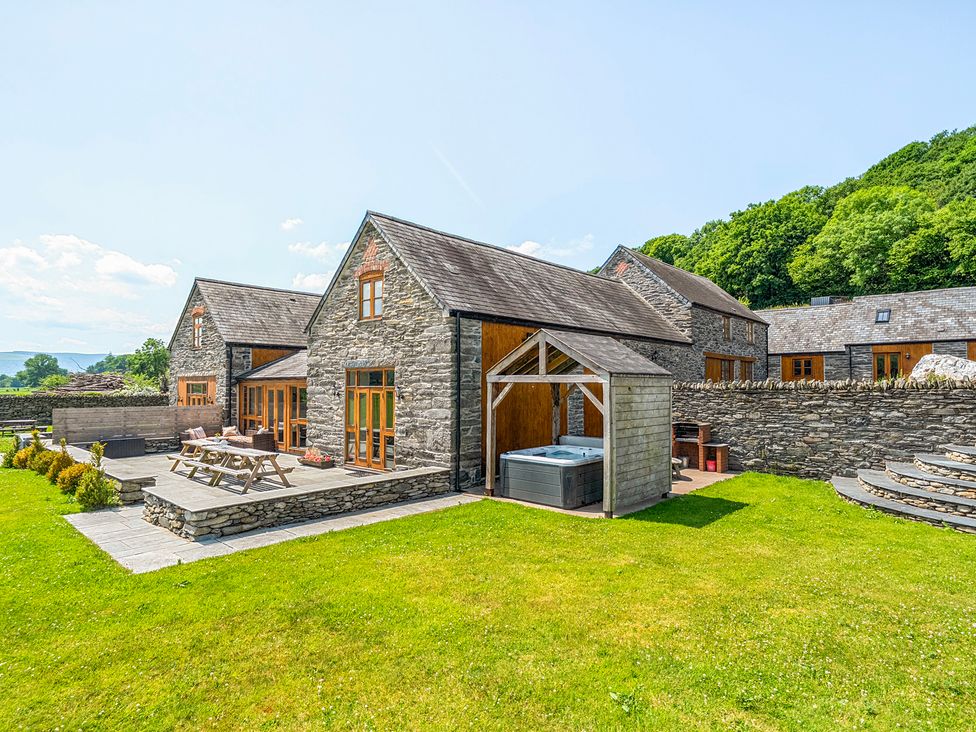 A house with a hot tub and patio furniture in the garden at The Barn in Corwen