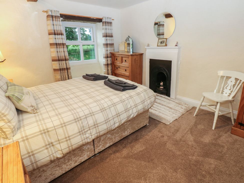 A bedroom with a bed, dresser, window, and fireplace at The LA'AL Cragg in Kirkby Stephen