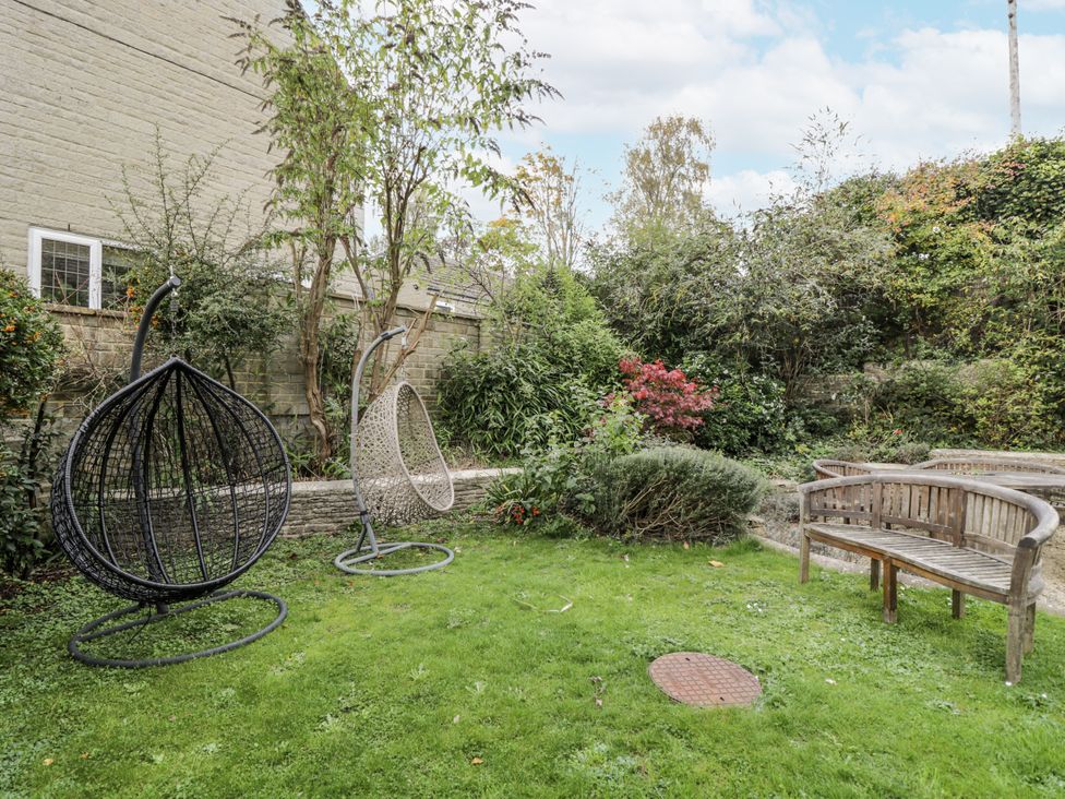 A garden with hanging chairs and a wooden bench at The Old Hall in Tetbury
