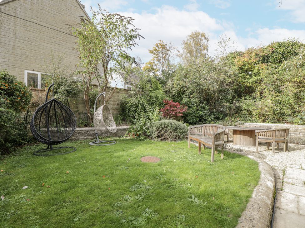 A garden with hanging chairs and a wooden table at The Old Hall in Tetbury
