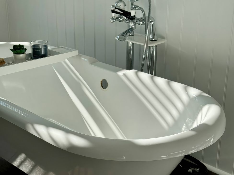 A bathtub with a faucet and a tray holding a plant at Port House in Lyme Regis