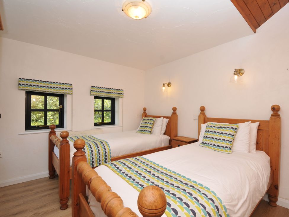 A bedroom with two beds and windows at Shipload Cottage in Hartland