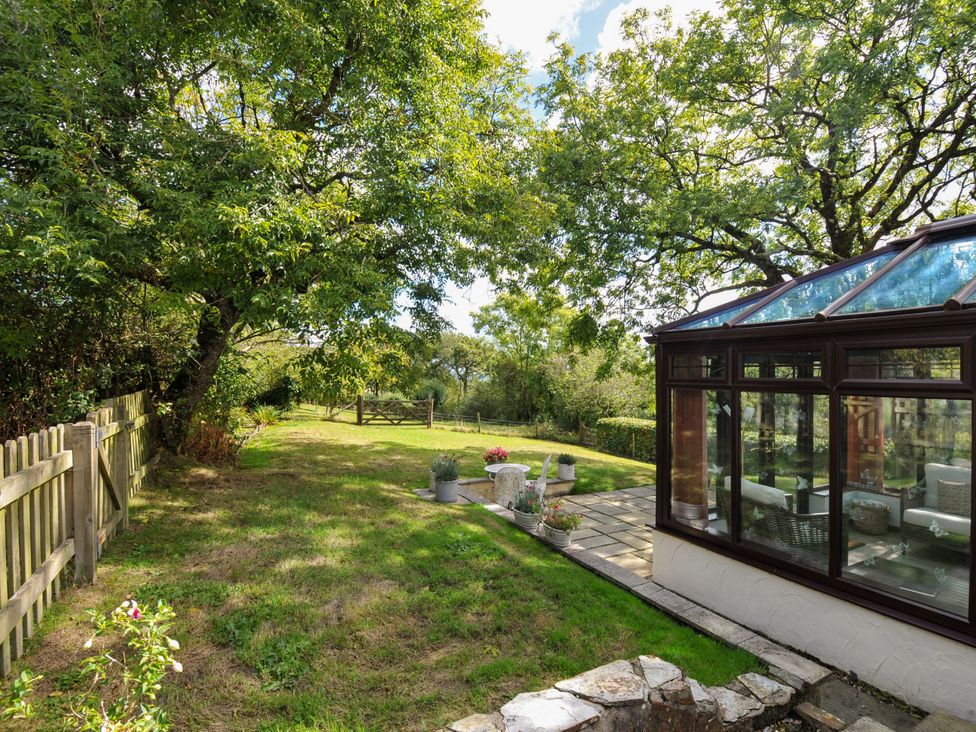 A garden with a conservatory and flower pots at Barley Cottage in Hartland