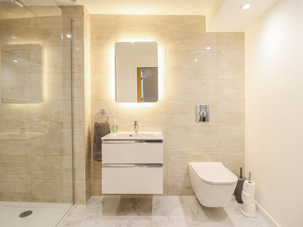 A bathroom with a shower, sink, mirror, and toilet at Neptune Cottage in Conwy