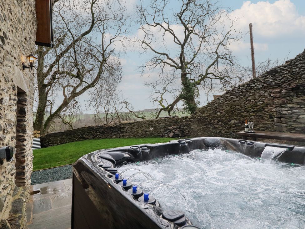 A hot tub with a view of a stone wall and trees at Godre'r Gyrn, Plas Moelfre Hall Barns, Oswestry