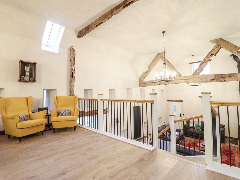 A living room area with yellow chairs and wood beams at Godre'r Gyrn, Plas Moelfre Hall Barns Oswestry