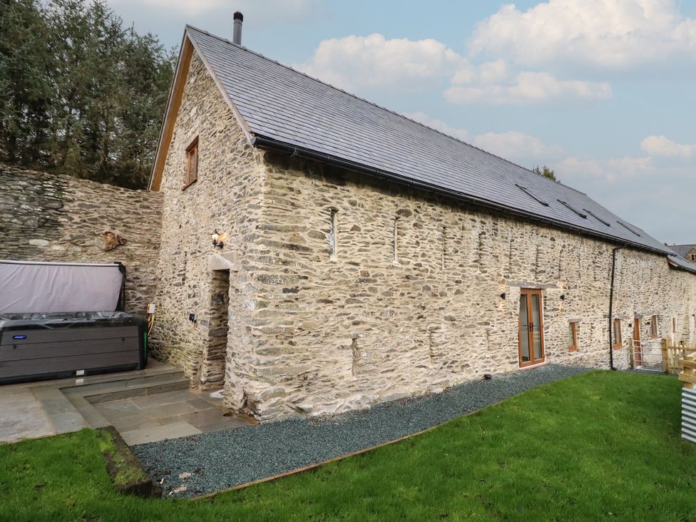 An outdoor view of a stone building with windows and hot tub at Godre'r Gyrn, Plas Moelfre Hall Barns, Oswestry