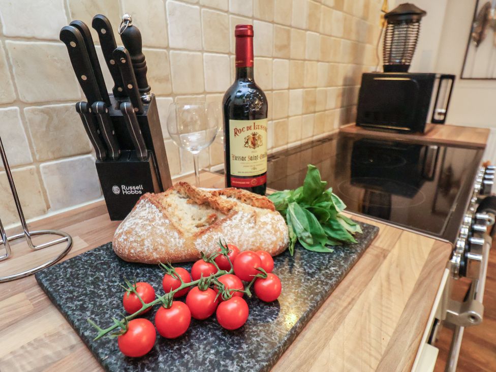 A kitchen with a cutting board, knives, wine, tomatoes, and bread at Honeysuckle in Filey