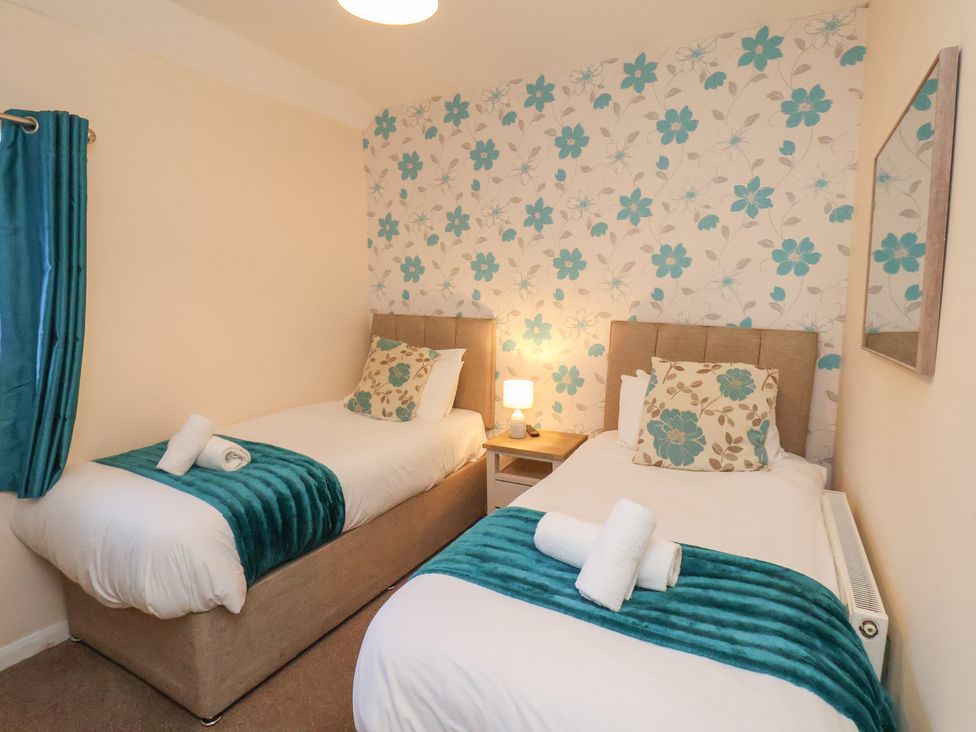 A bedroom with two beds and a bedside table at Honeysuckle in Filey
