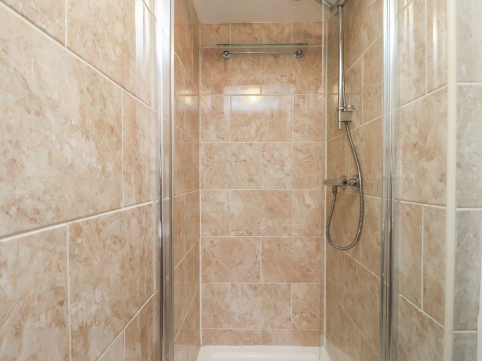 A shower area with tiles and showerhead at Honeysuckle in Filey