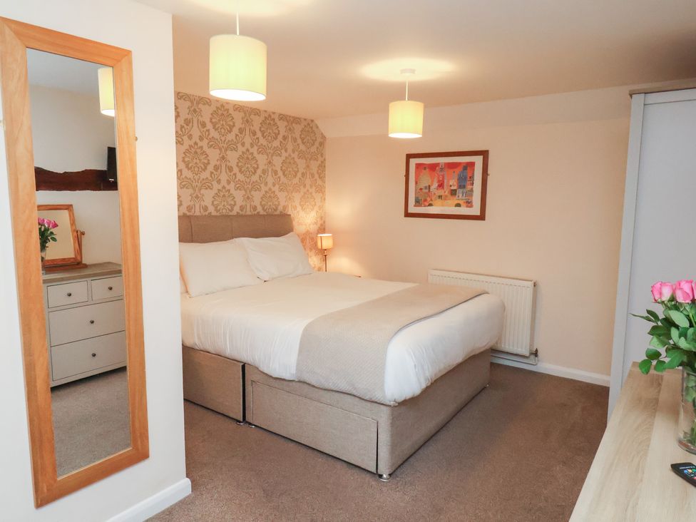 A bedroom with a bed, mirror, and dresser at Honeysuckle in Filey