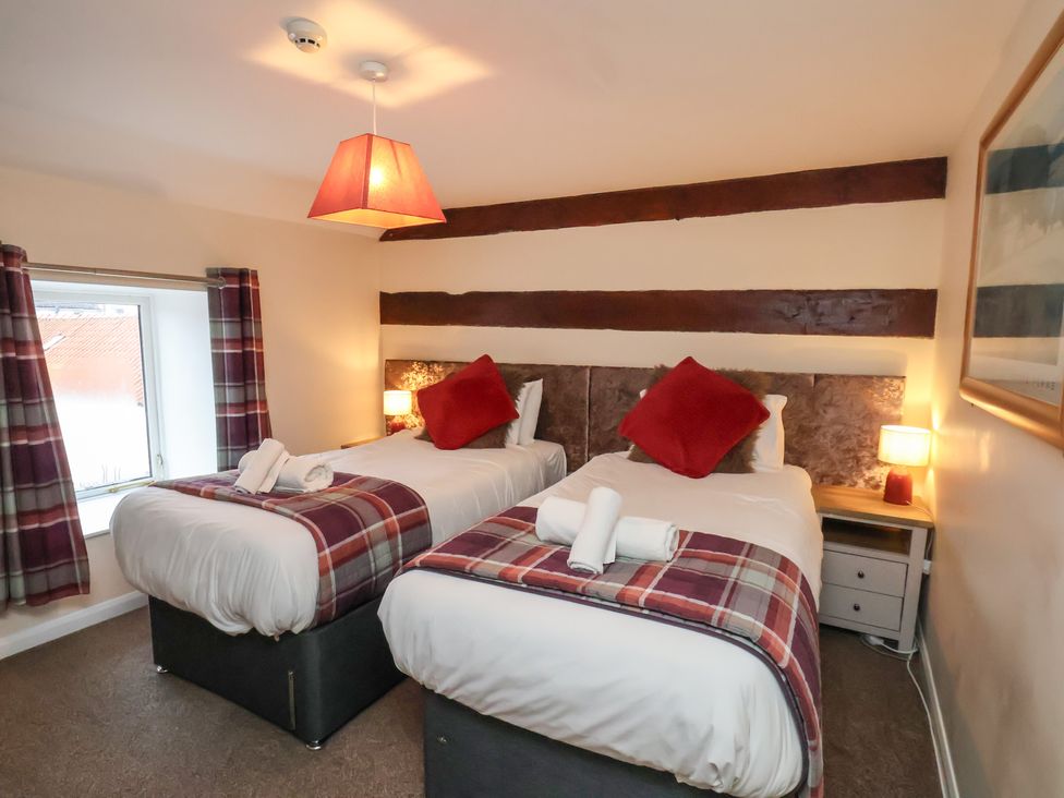 A bedroom with two beds and a bedside table at Honeysuckle in Filey
