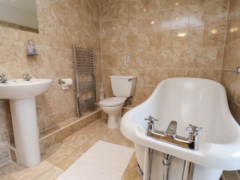 A bathroom with a bathtub, toilet, sink, and towel rack at Honeysuckle in Filey