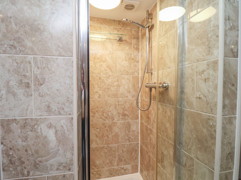 A shower area with tiled walls and shower fixtures at Honeysuckle in Filey