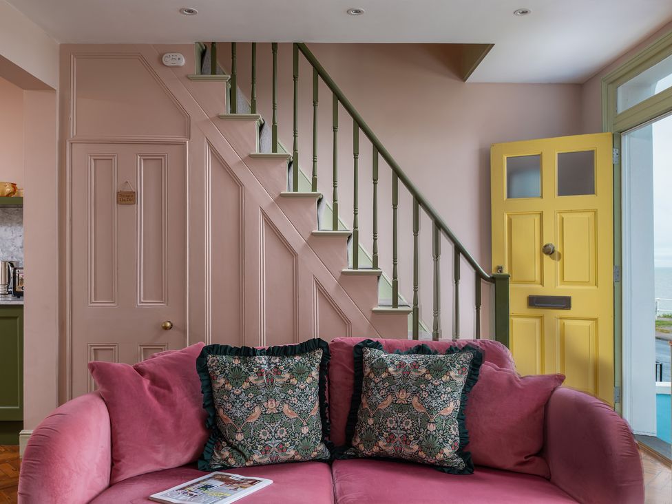 A living room with a pink sofa and yellow door at Astondene, East Cliff in Southwold