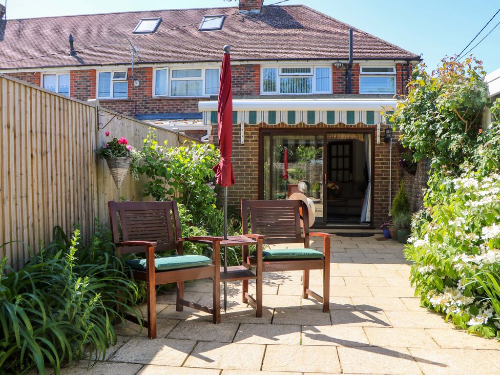 A garden patio with two wooden chairs and a closed umbrella between them at Lavender Cottage in Hailsham