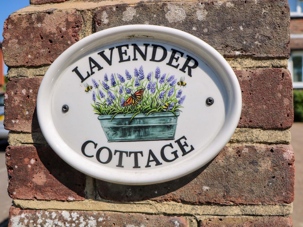 A sign with lavender flowers and bees on a brick wall at Lavender Cottage in Hailsham